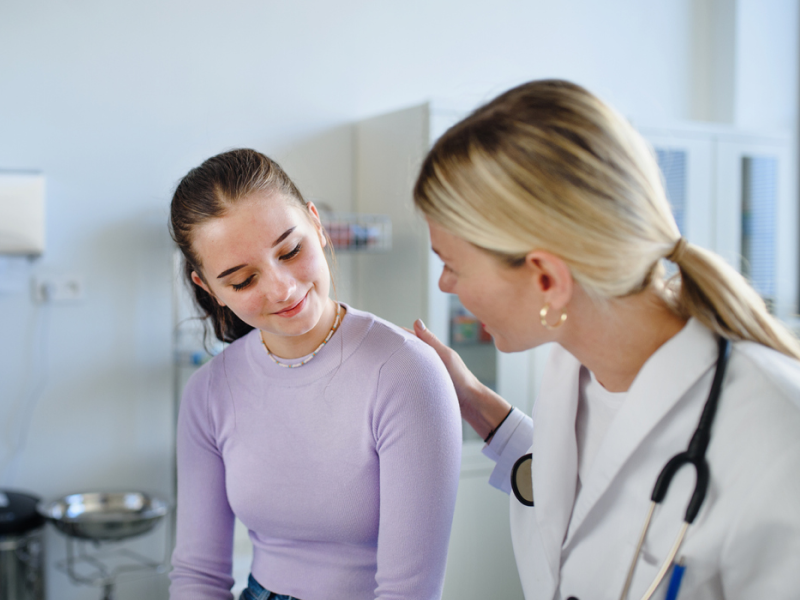 صورة لامرأة مبتسمة في عيادة تجميل بعد انتهاء جلسة، مع طبيب يشرح لها النتائج.